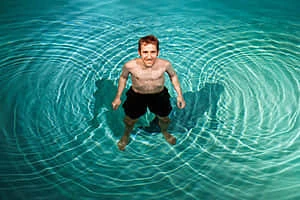 プールの水面に広がる波紋と水中に立つ人の写真。